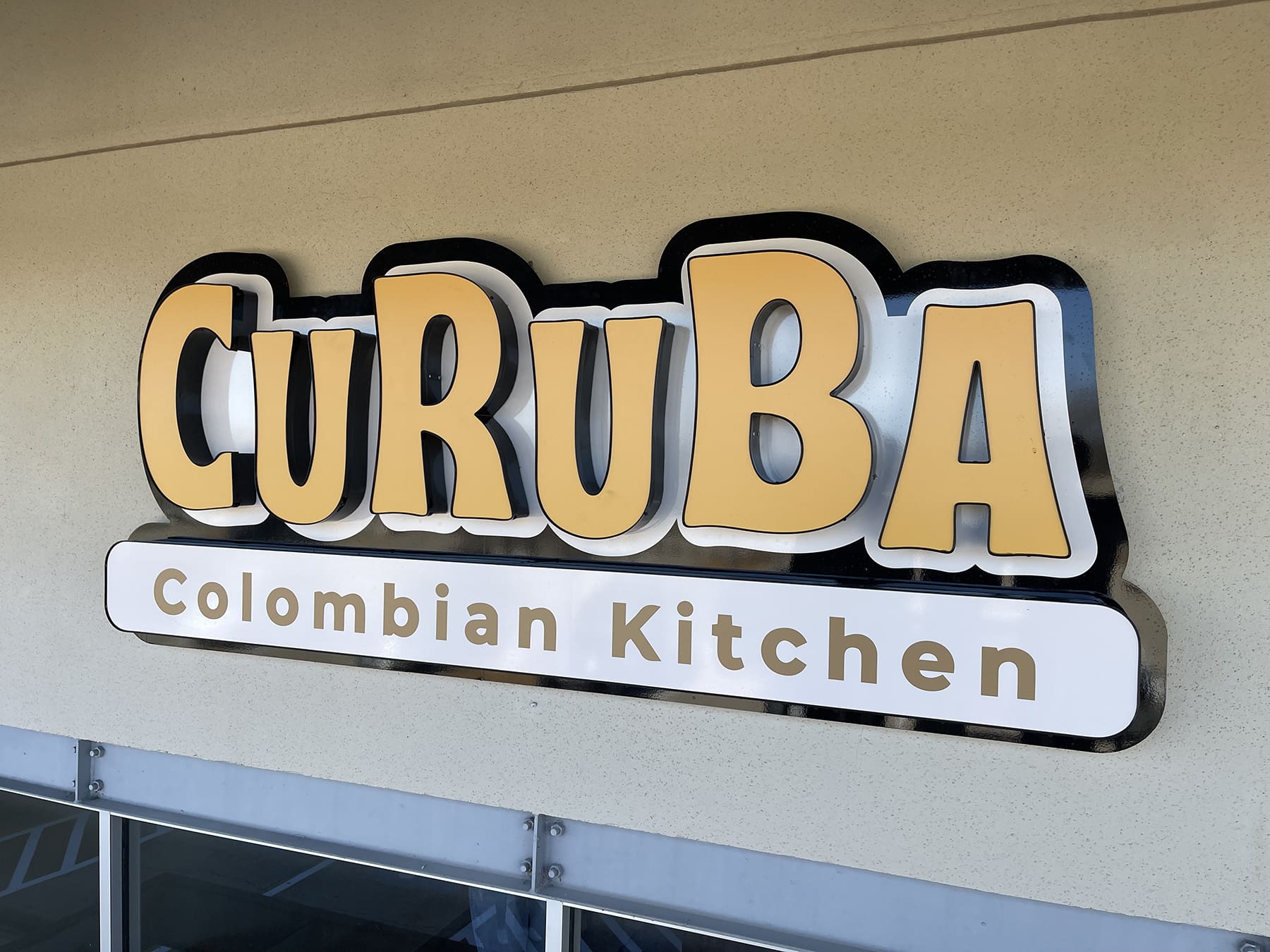 An outdoor electrical storefront sign with stylized yellow and black letters spelling 'CURUBA' above smaller text reading 'Colombian Kitchen'.